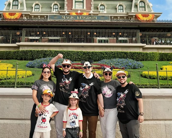Grupo familiar con gorras de Disney posando frente a la entrada de Magic Kingdom durante el día.