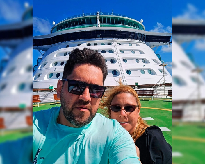 Pareja posando en la cubierta de un crucero con vista a la estructura principal del barco.